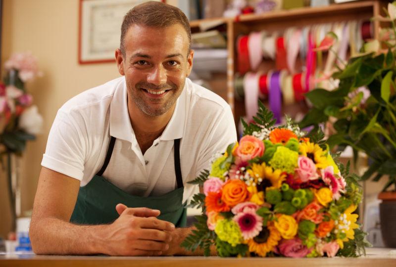 微笑的男人站在花店多彩的花束旁
