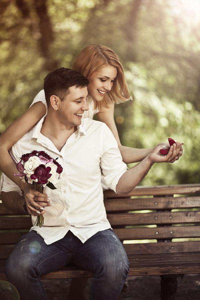 年轻的情侣坐在公园里男人手里拿着戒指向女人求婚