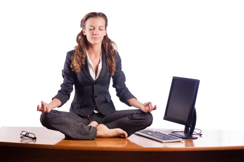 白色背景下坐在办公桌上练习瑜伽的女人