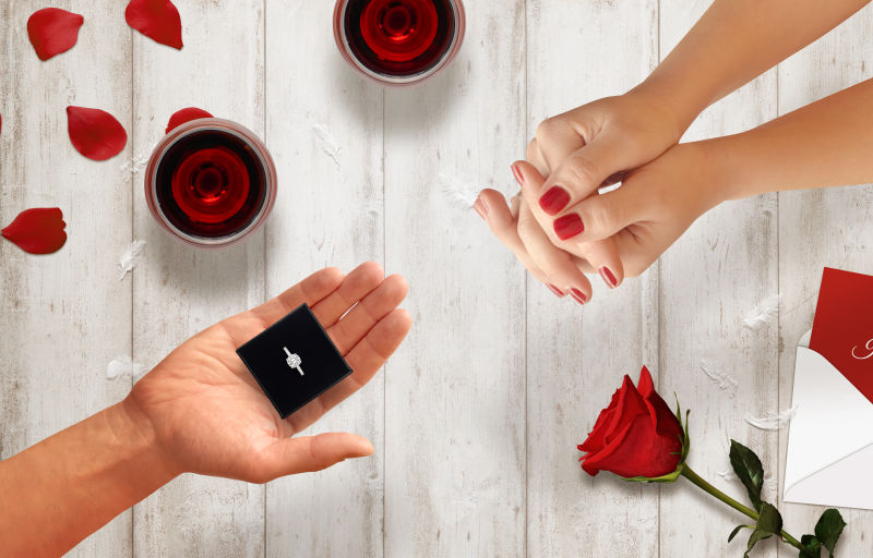 有玫瑰信封在木桌上男人把订婚戒指交给女性手