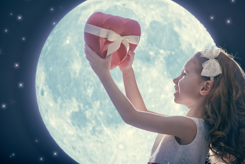 举高红心礼盒的小女孩在月亮的背景下