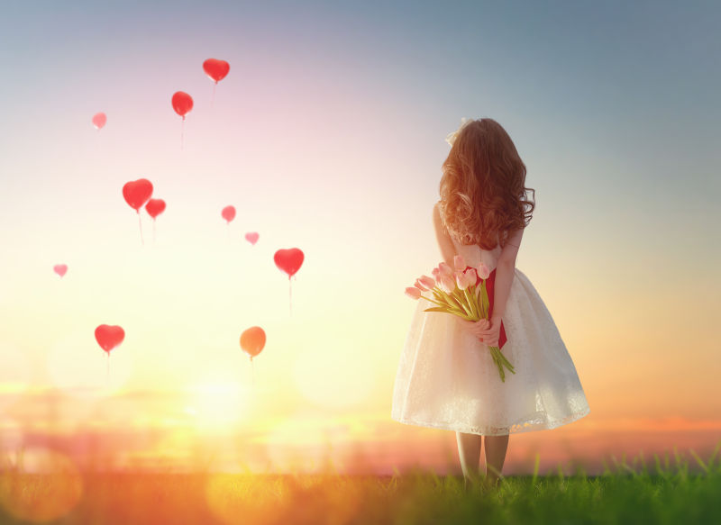 小女孩背后拿着花束看着前方太阳下的红心