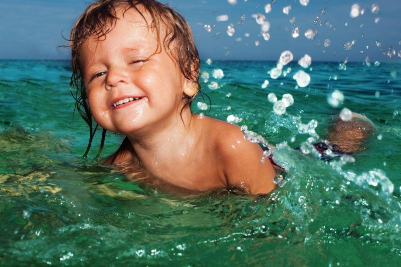 快乐的两岁小孩在海水中游泳和溅水