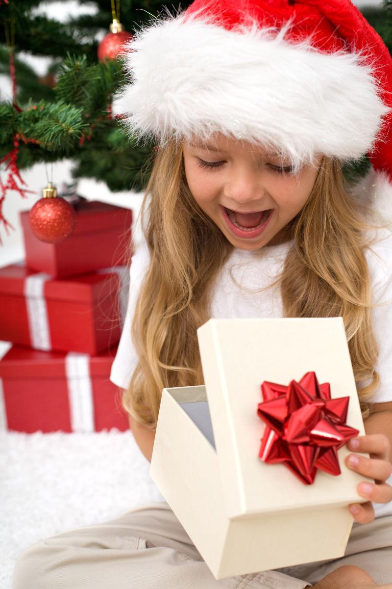 圣诞树旁抱着礼品盒的孩子