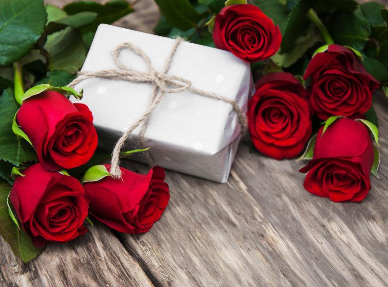 红玫瑰和木桌上的白色礼品盒