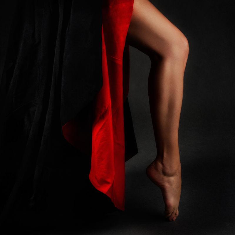黑色背景下穿着红裙子的腿