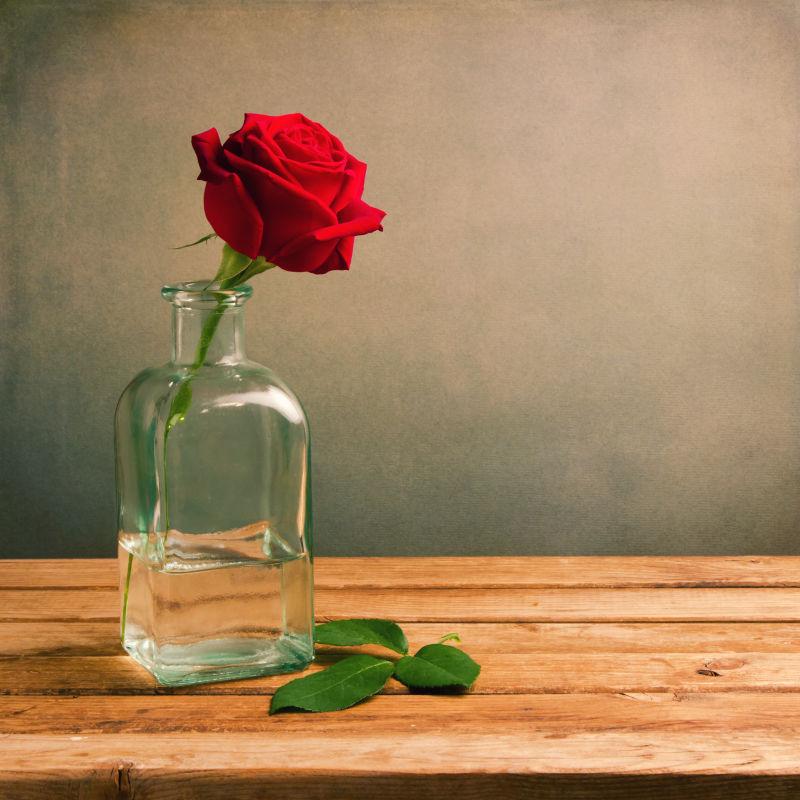 木桌上玻璃瓶中的红玫瑰