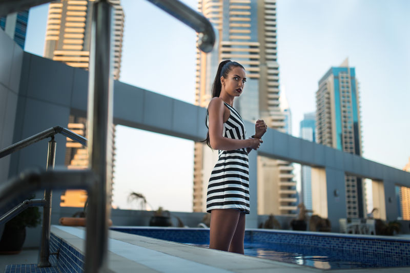 摩天大楼背景上站在泳池里的年轻女人