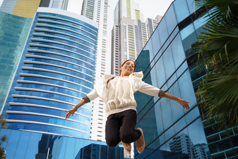 在商业办公大楼和摩天大楼旁边跳跃的年轻女人