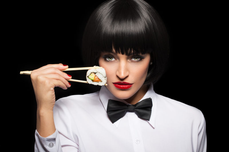 黑色背景上的美女夹着一个寿司