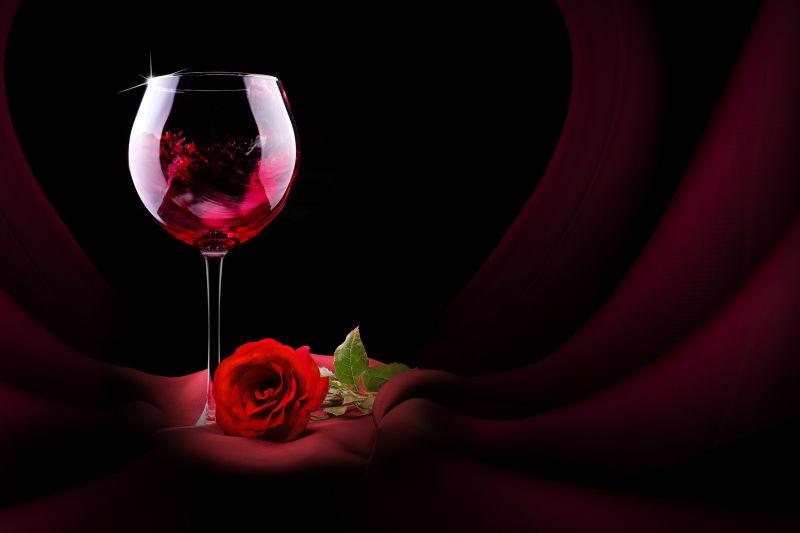 黑色聚光背景一杯红酒与红玫瑰