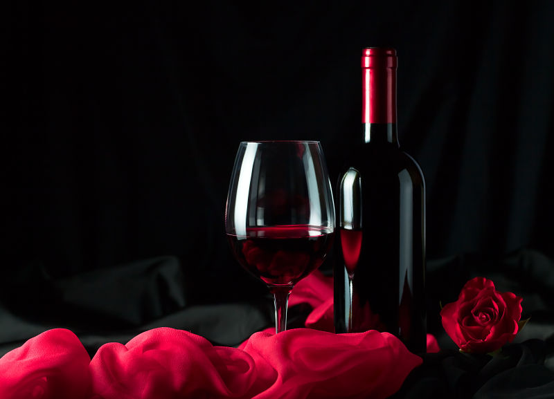 黑背景中的一杯红酒与玫瑰花朵