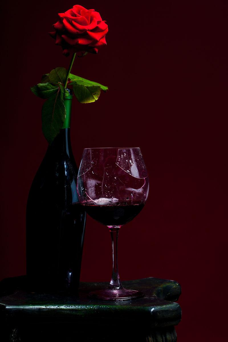 黑背景中的酒瓶里的红玫瑰和一杯红酒