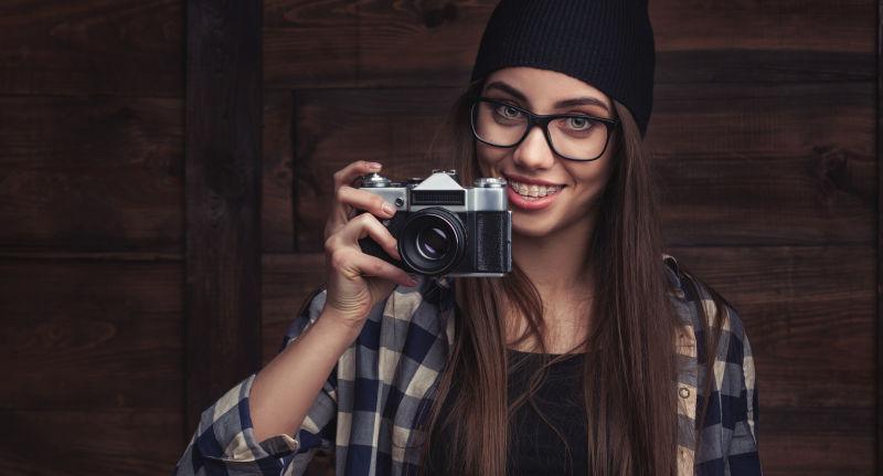 木制背景上戴眼镜和照相机的时髦女孩