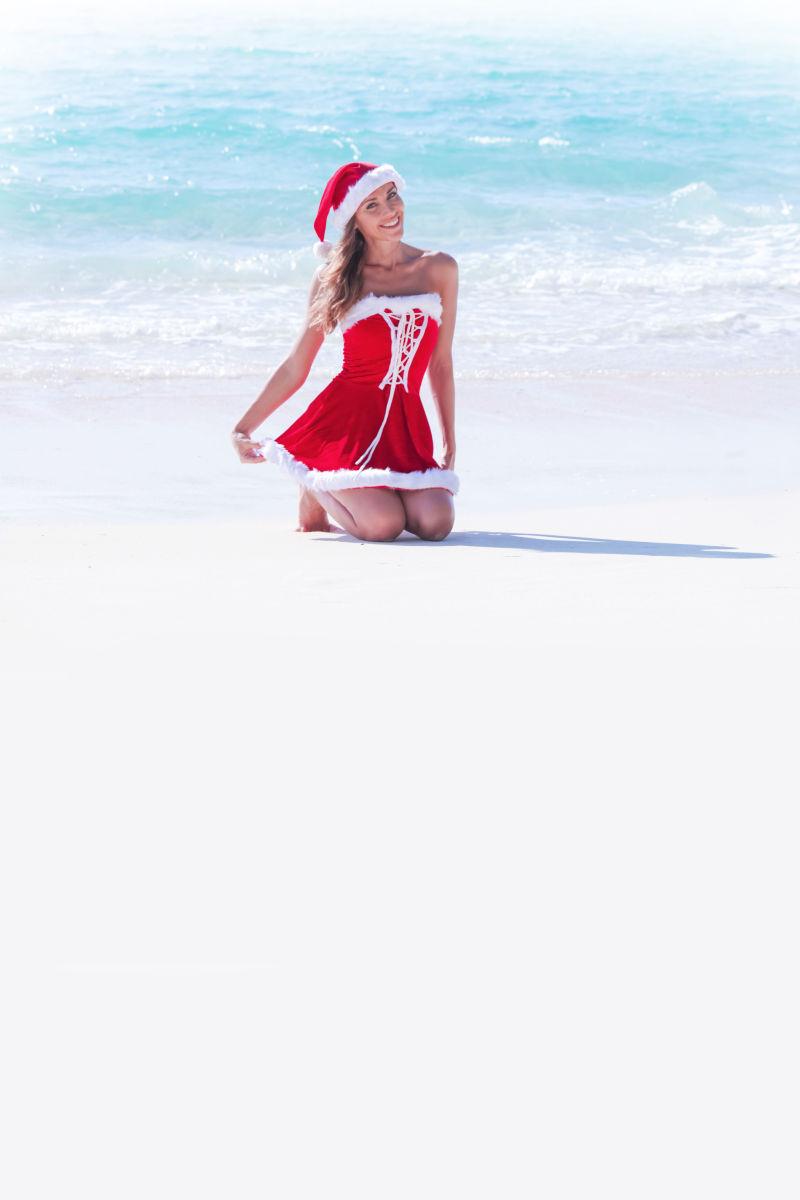 蓝色大海边穿着圣诞老人衣服跪坐在沙滩上的女士