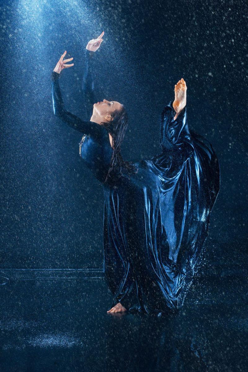 美丽的现代舞者穿着蓝色长裙在雨中舞蹈