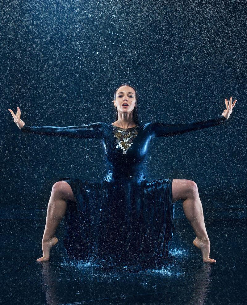 年轻美丽的现代舞蹈家穿着蓝色长裙在雨中跳舞