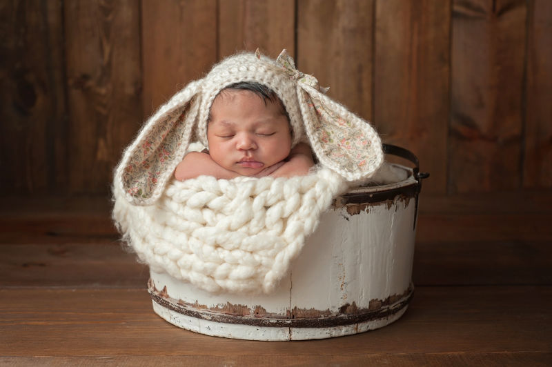 戴着兔耳朵帽子在白色木桶里睡觉的婴儿