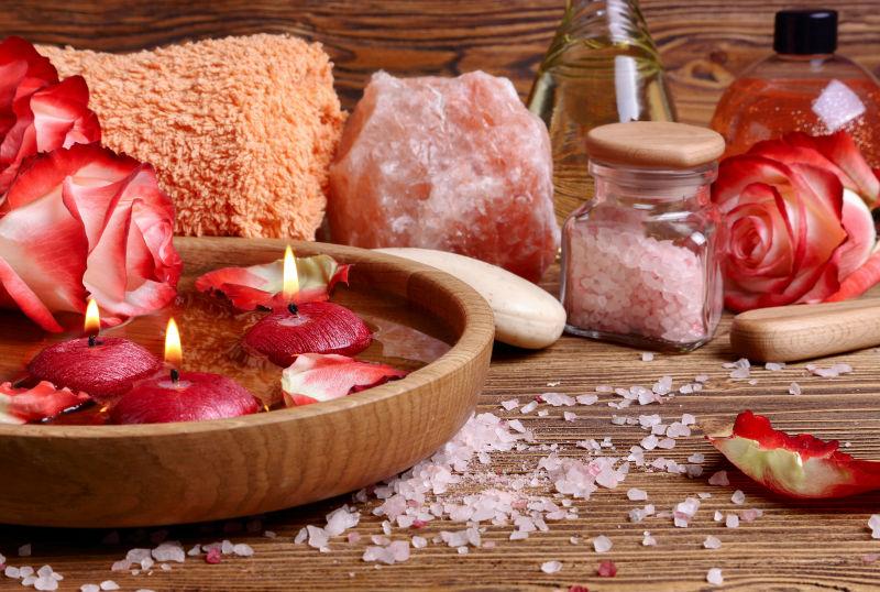 粉红盐和蜡烛漂浮在木制的碗里在木桌上
