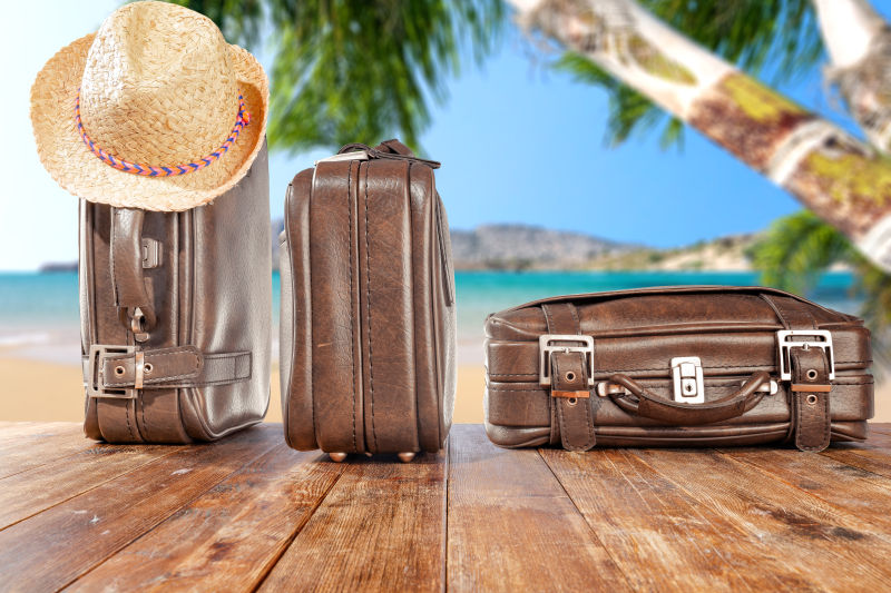 海滩背景下放在木板上的三个旅行手提箱