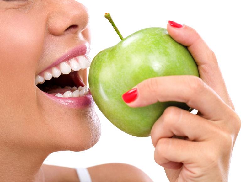 白色背景下拿着绿色苹果露着牙齿微笑的人