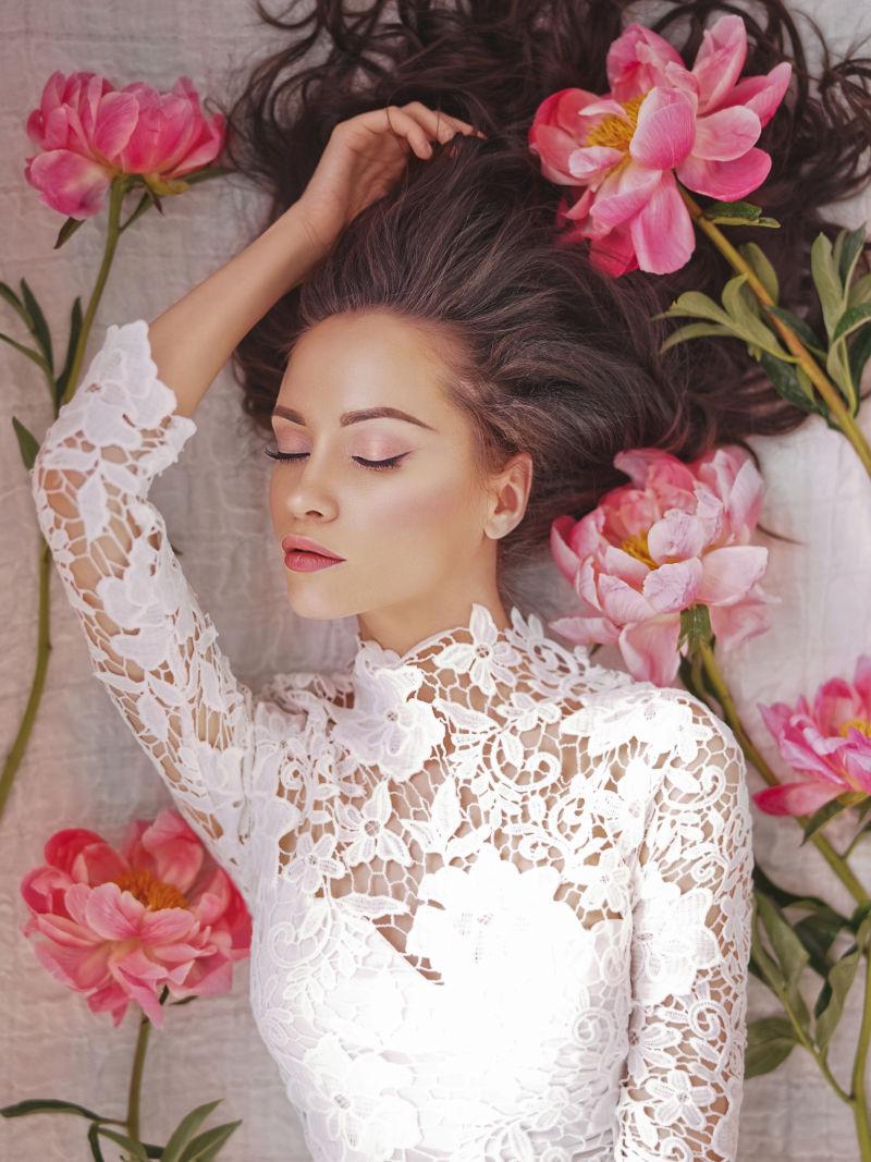 穿着白色蕾丝衣服的美女躺着牡丹花中间