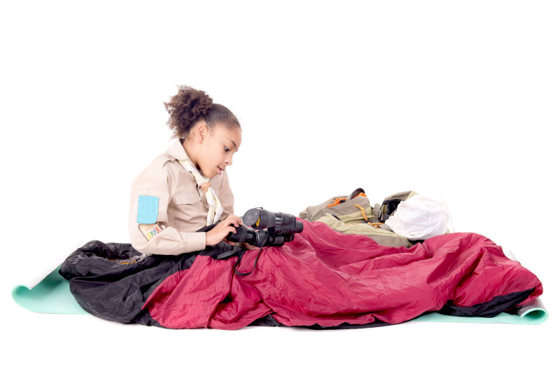 白色背景上拿着望远镜坐在睡袋里的小女孩