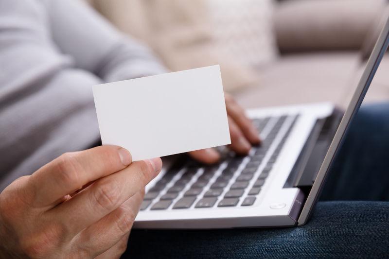 商人在使用笔记本电脑时手持一张空白的白色卡片