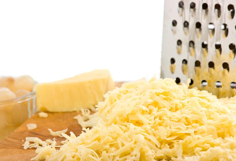 磨碎的软切达干酪在木板上用磨碎机