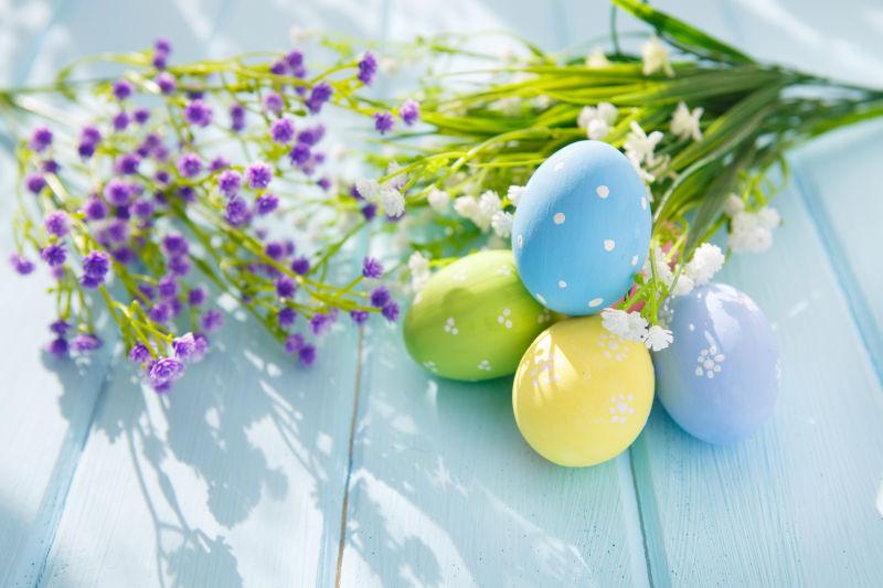 淡蓝色木桌上的复活节彩蛋和紫色白色的满天星花朵