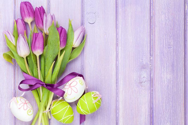 淡紫色木桌上的紫色郁金香花束和复活节彩蛋