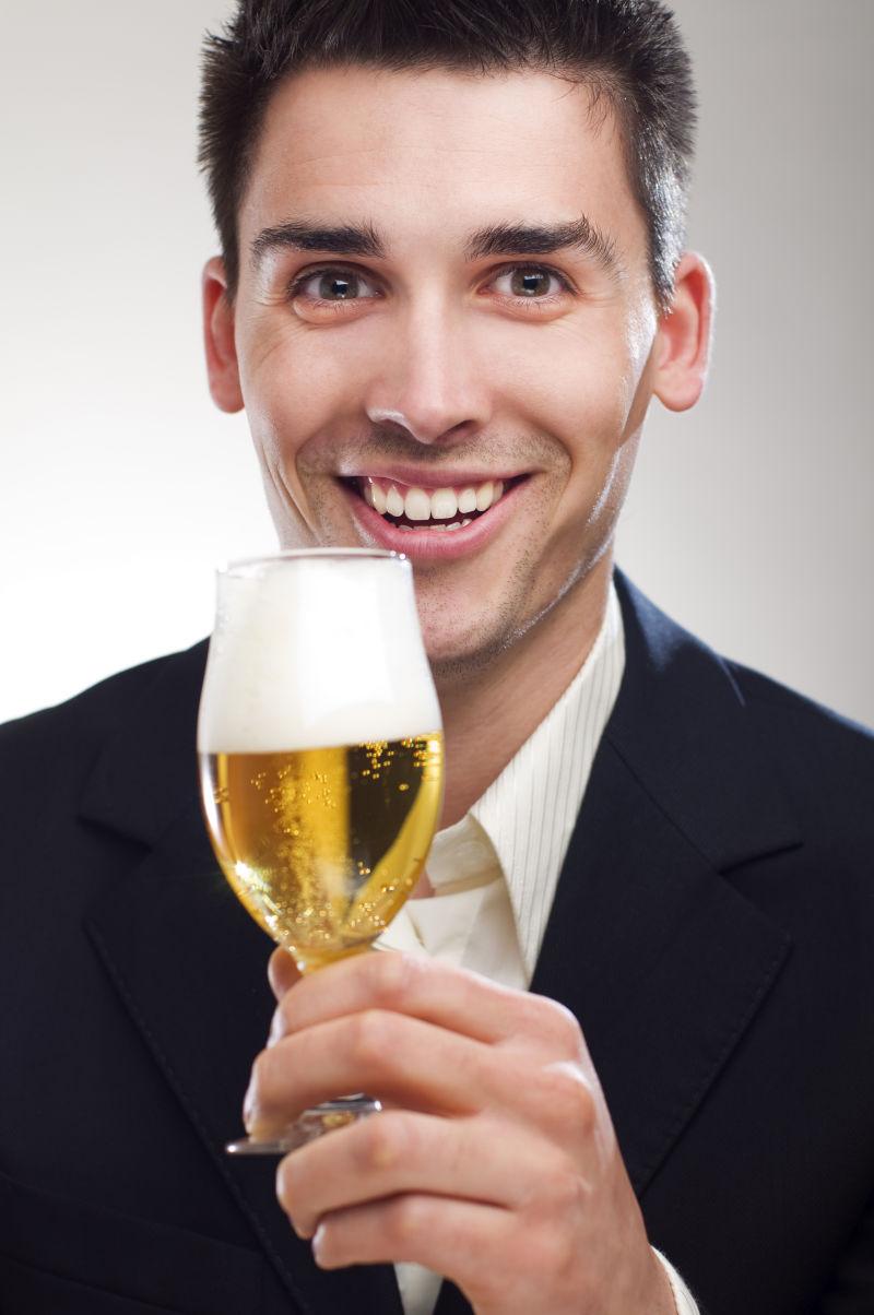 灰色背景上端起啤酒杯微笑的穿着西装的男人