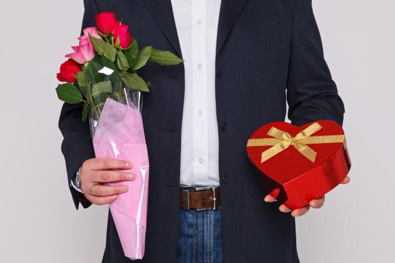 男人拿着一束鲜花和一盒心形的巧克力盒子