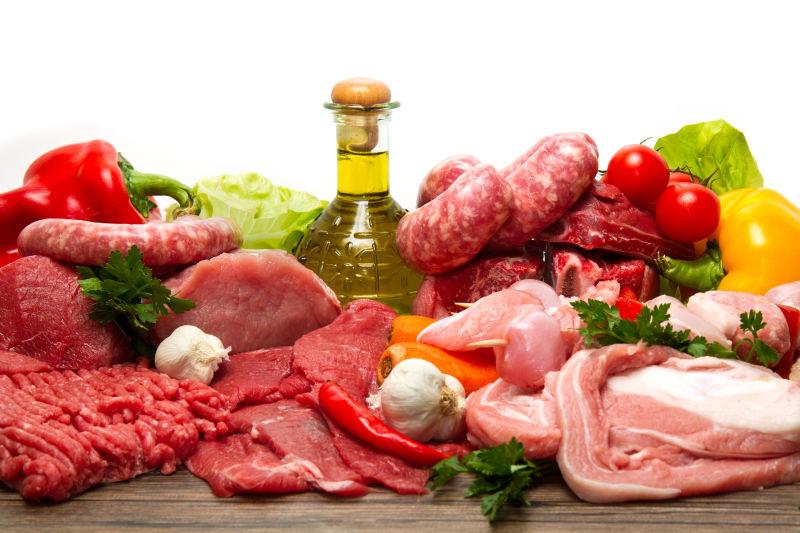 白色背景下的蔬菜旁的一堆生肉和生肉制品