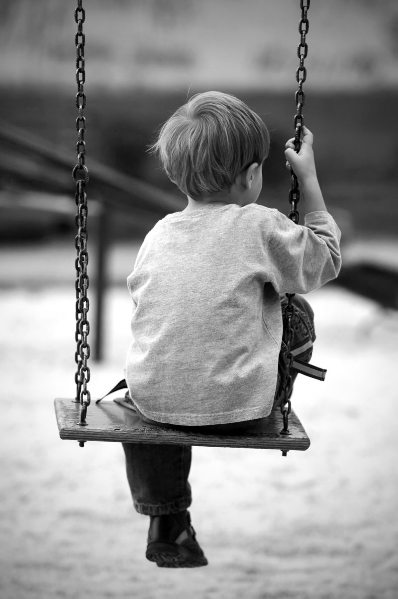 黑白背景下公园里坐在秋千上的孤独男孩