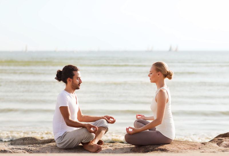 海边年轻的夫妇正在做瑜伽