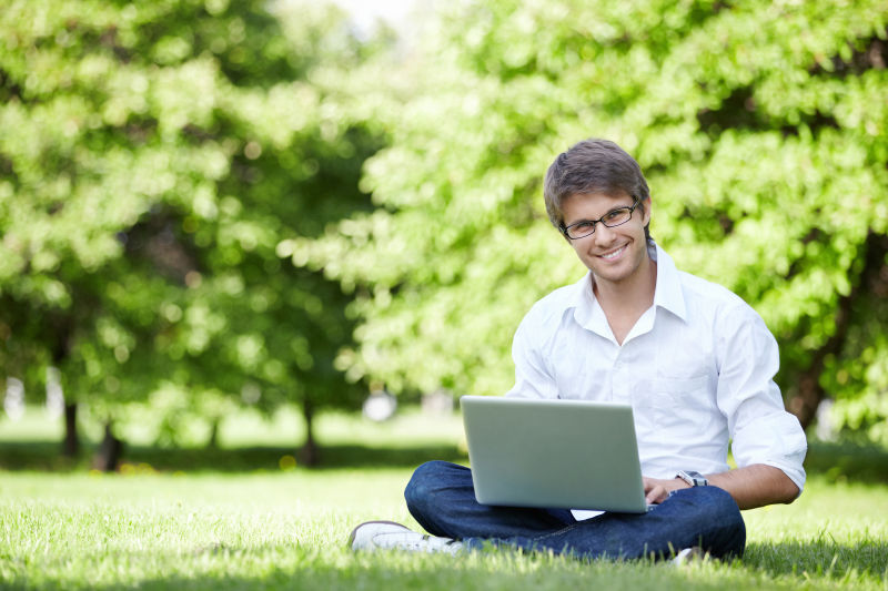 坐在草坪上的帅哥使用笔记本电脑