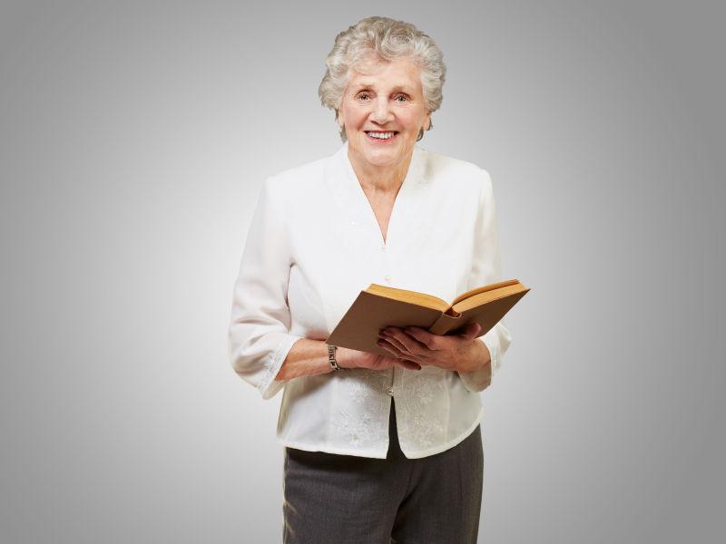 灰色背景下双手捧着书的微笑的老奶奶