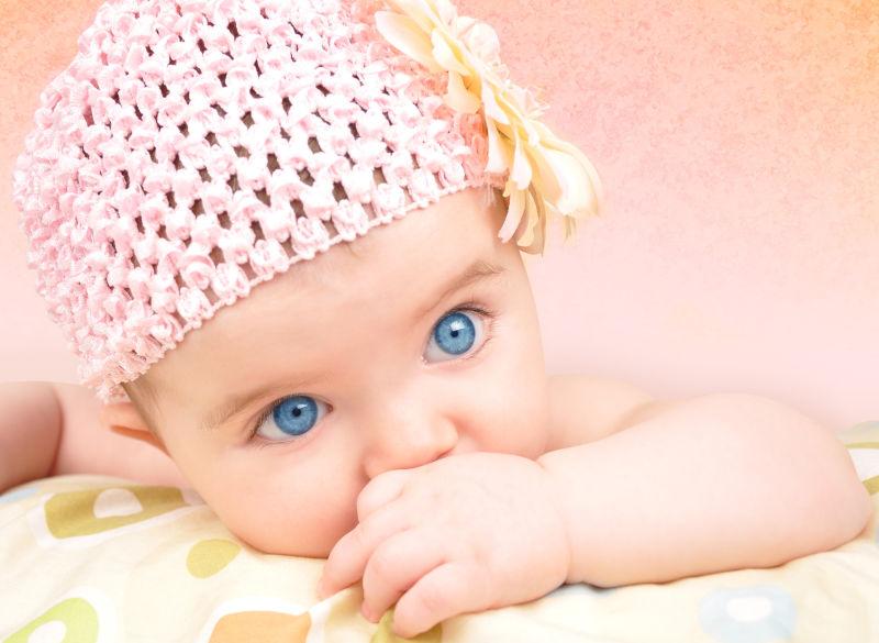 趴在枕头上带着粉色编织帽子的小婴儿