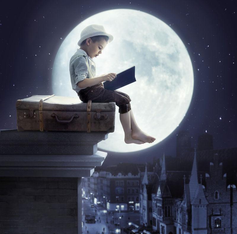 屋顶上坐在行李箱月亮前的小男孩
