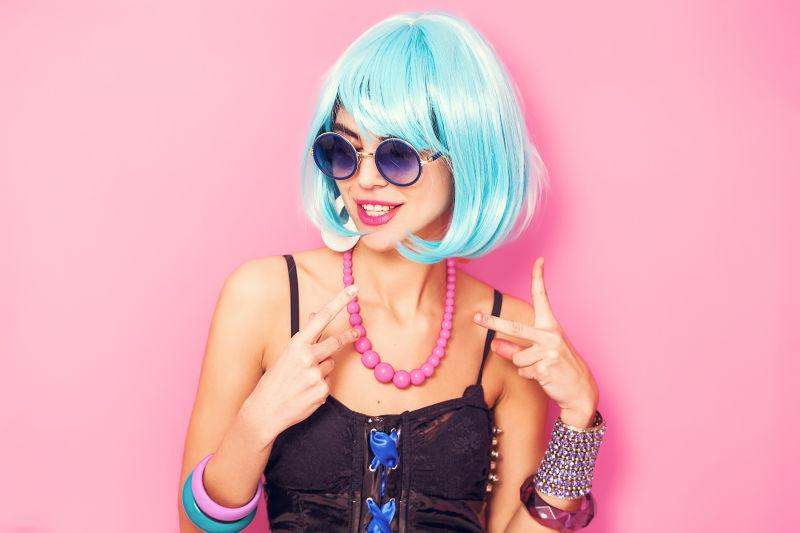 粉色背景下戴着浅蓝色假发比剪刀手的时尚美女