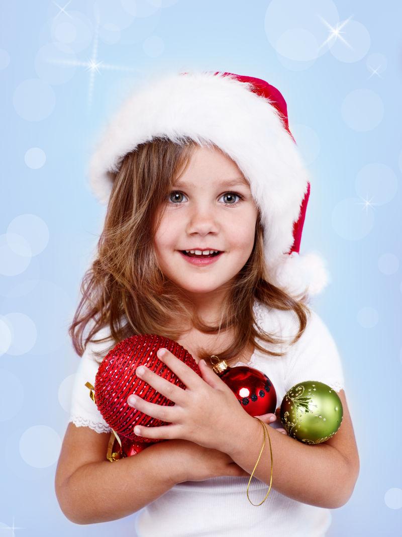 抱着装饰球带着圣诞帽的小女孩