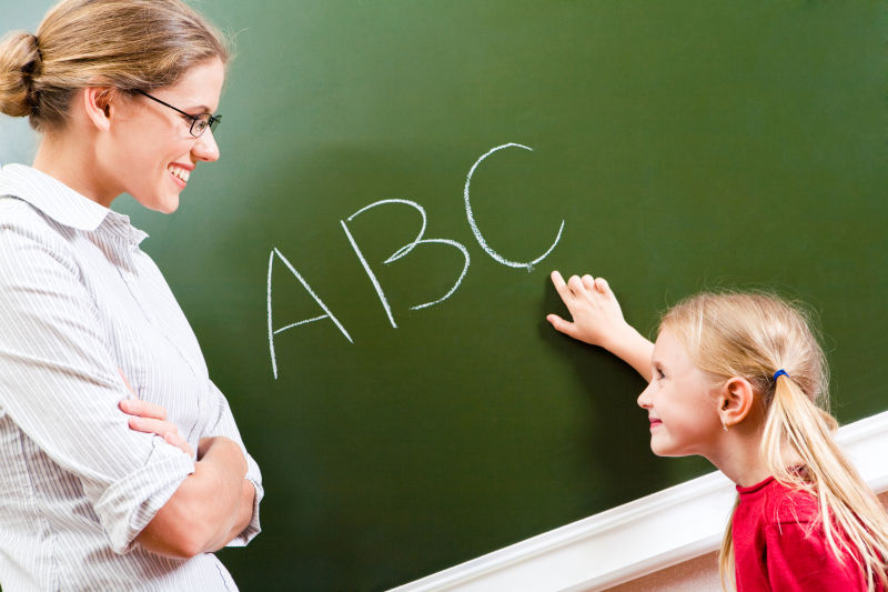 聪明女孩在黑板上指着字母微笑着看着老师