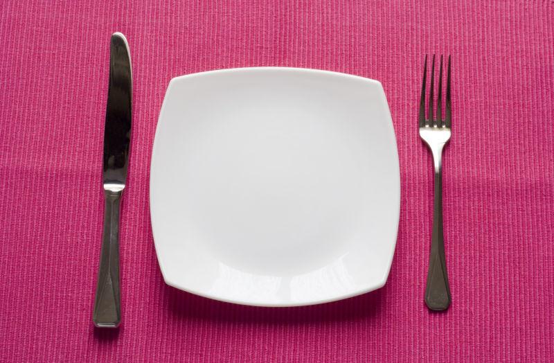 粉色背景上的白色餐盘和刀叉