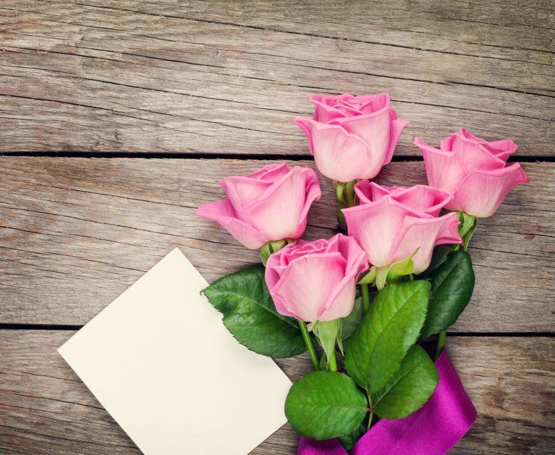 在木桌上粉红玫瑰和空白贺卡