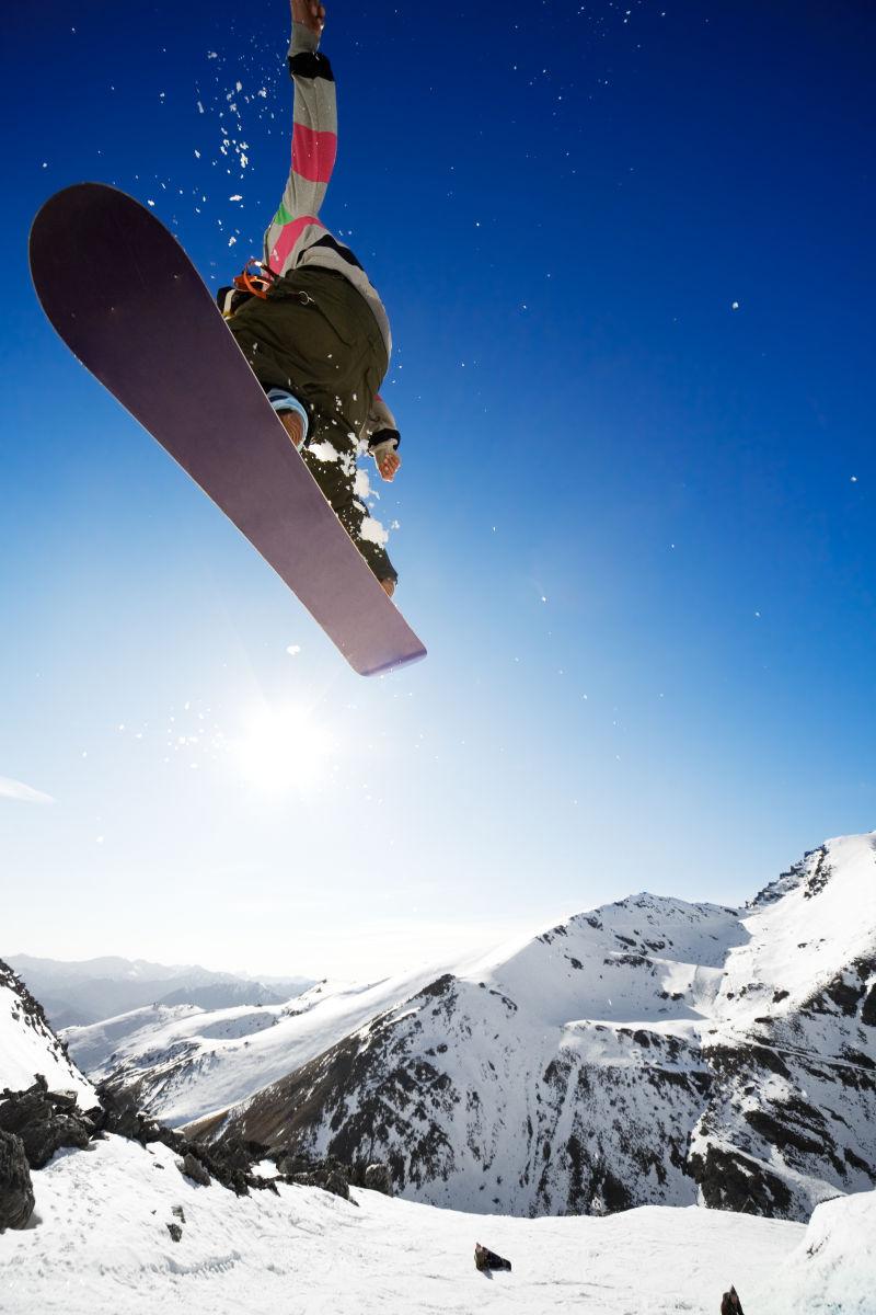 蓝色天空背景上的雪山上踩着滑雪板跳起来的人