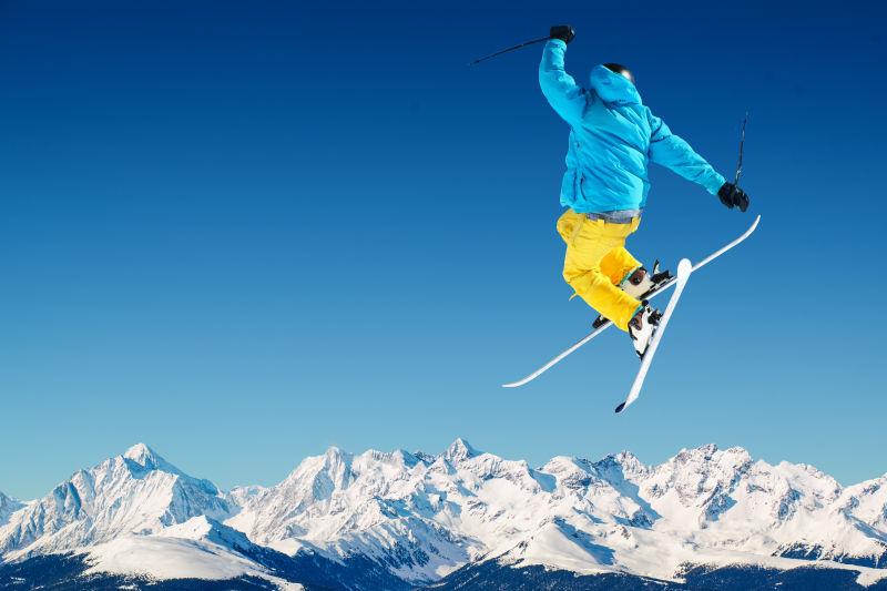 蓝天下的群山背景下跳起来的滑雪人
