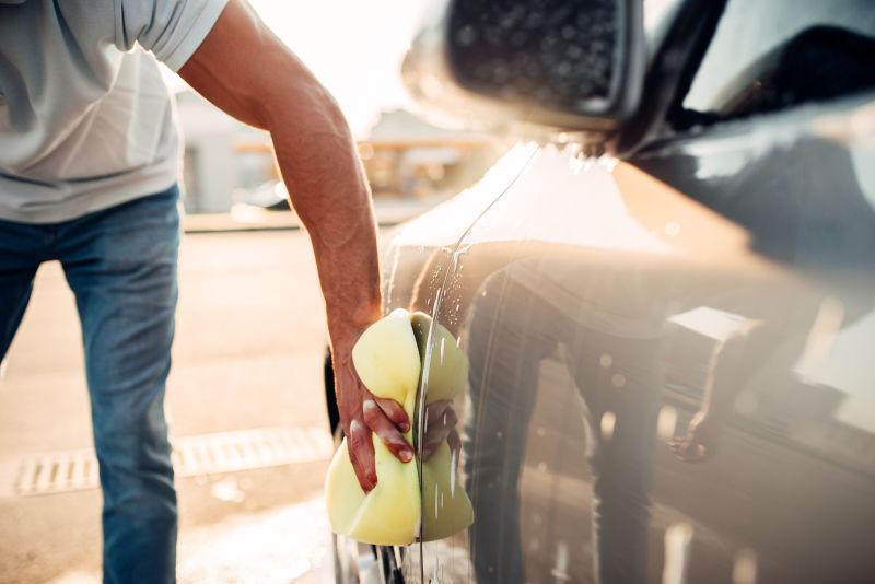 阳光下的男子用泡沫海绵擦洗汽车