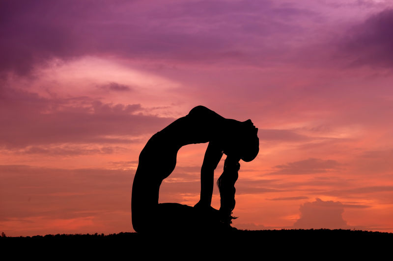 日落时分往后仰头做瑜伽动作的女子剪影