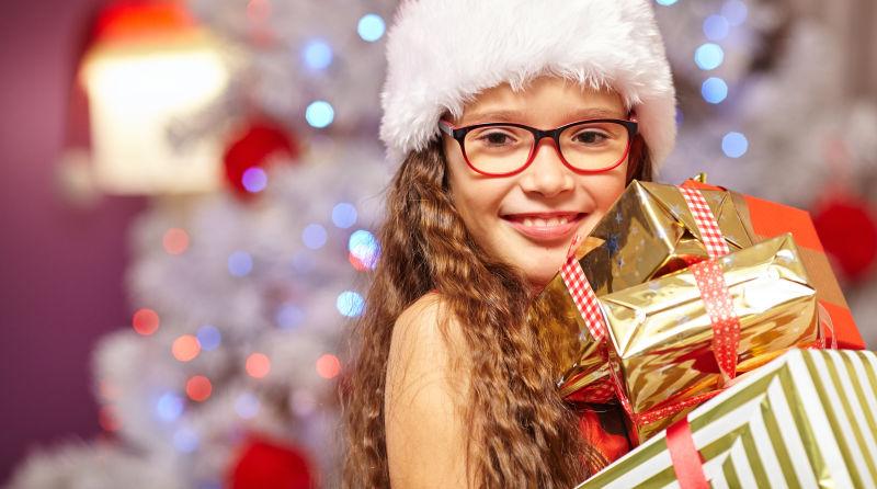 在圣诞树前微笑的女孩拿着礼物